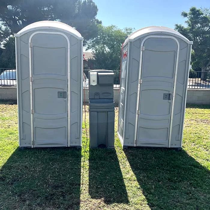 Two portable toilets with an exterior handwashing station set up together on grass